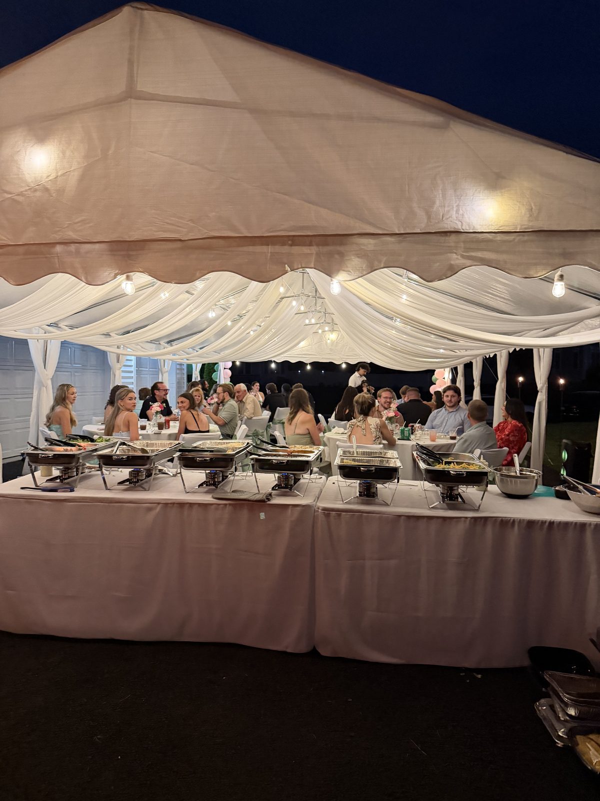 Guests seated for dinner under a lit tent in the evening