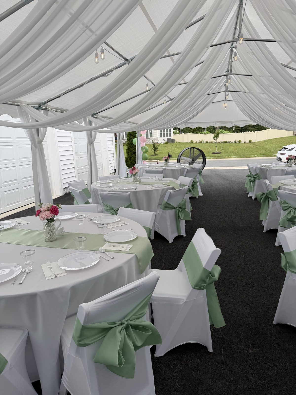 Round tables set with linens, chair sashes, and floral centerpieces under a tent